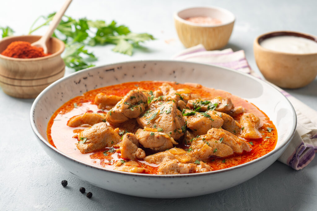 Chicken stew with paprika, onion and sour cream in plate on concrete background. Traditional Hungarian dish Paprikash. Selective focus.